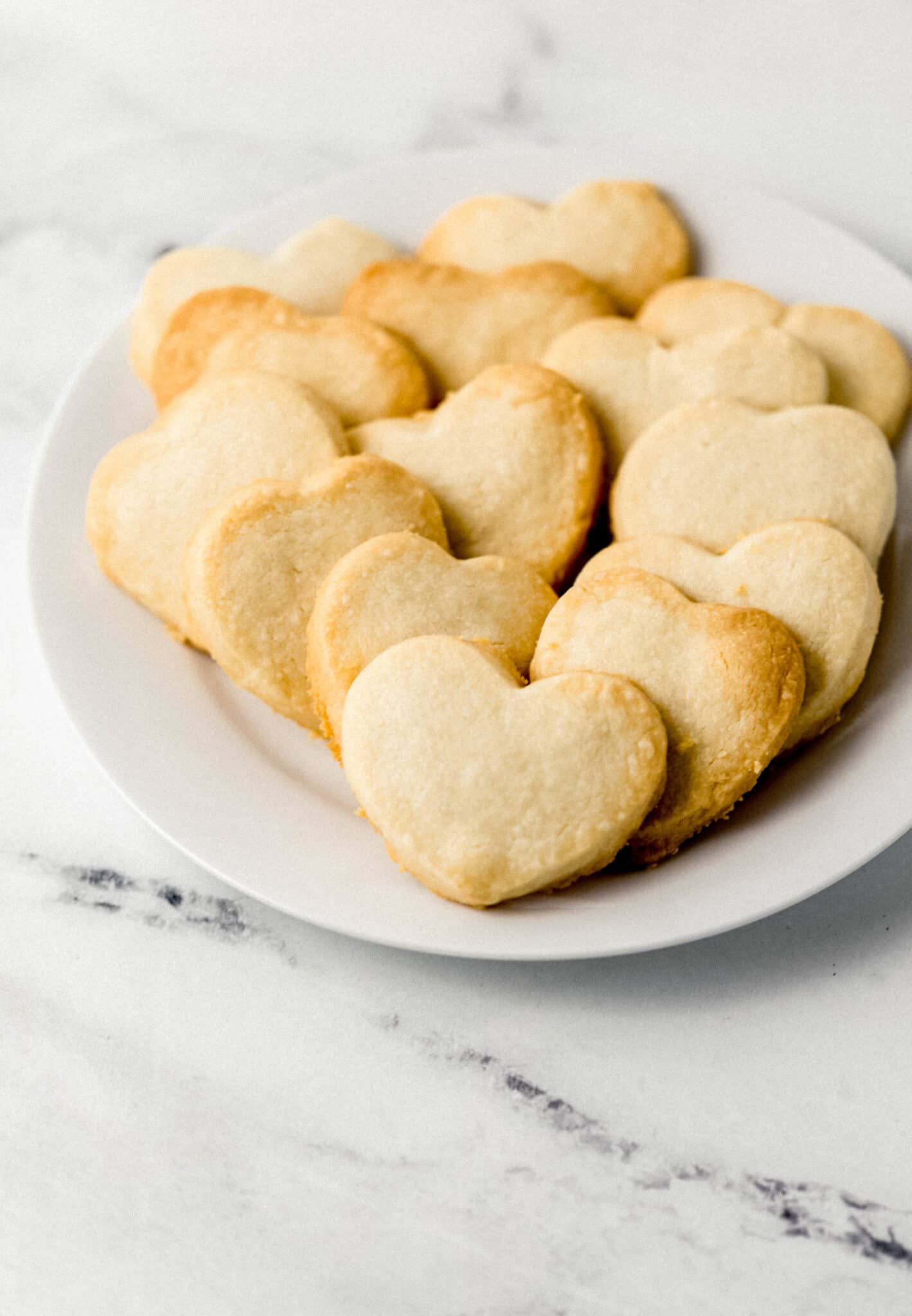 close up side view of white plate of heart shaped shortbread cookies 