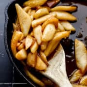 Close up front view of finished apples in cast iron skillet on black tile surface.