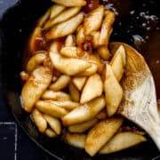 Fried apples in cast iron skillet with wooden spoon in them.