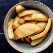 Overhead view of single serving of fried apples in a grey bowl by a fork.