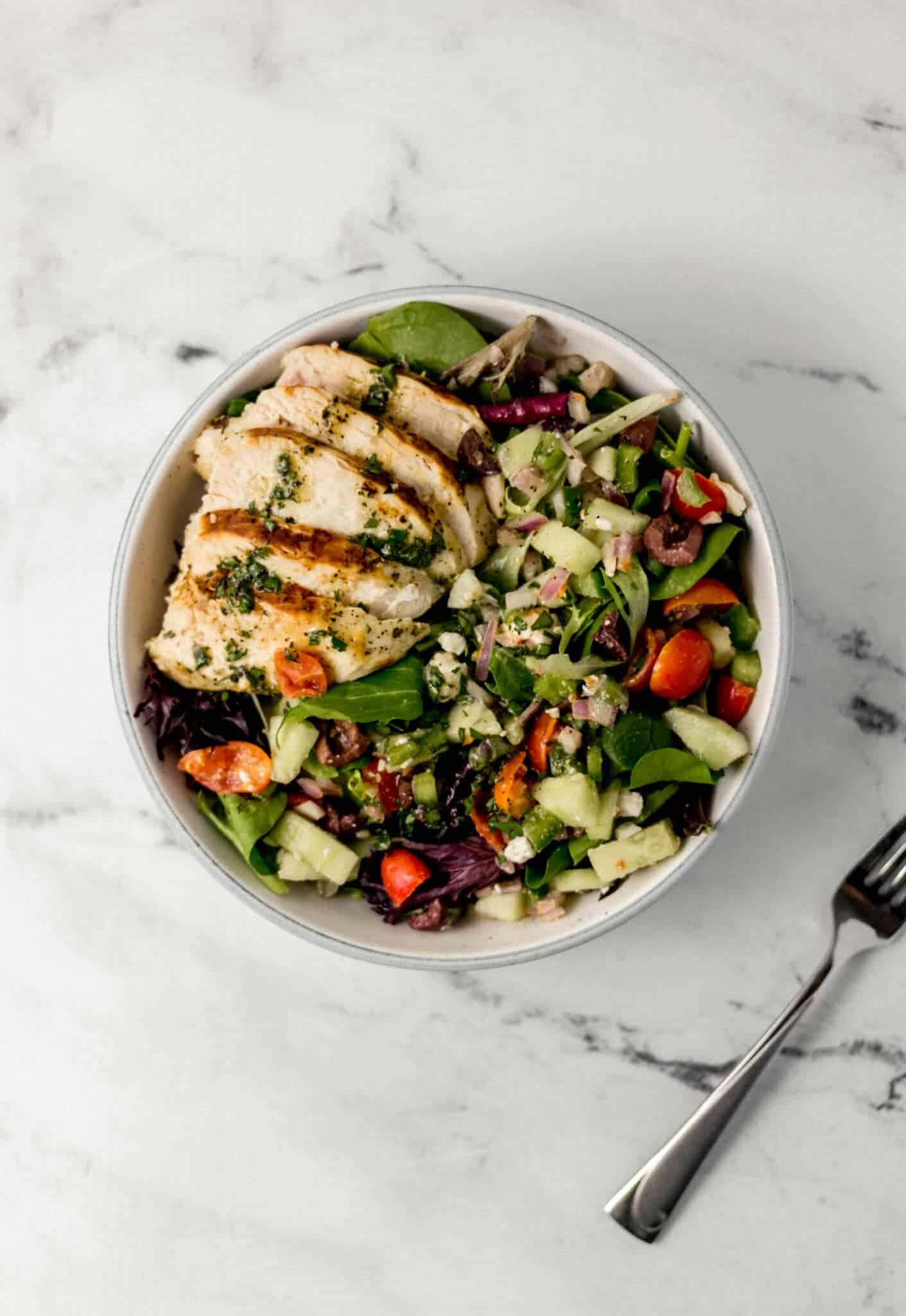 overhead view of finished salad in white bowl by fork
