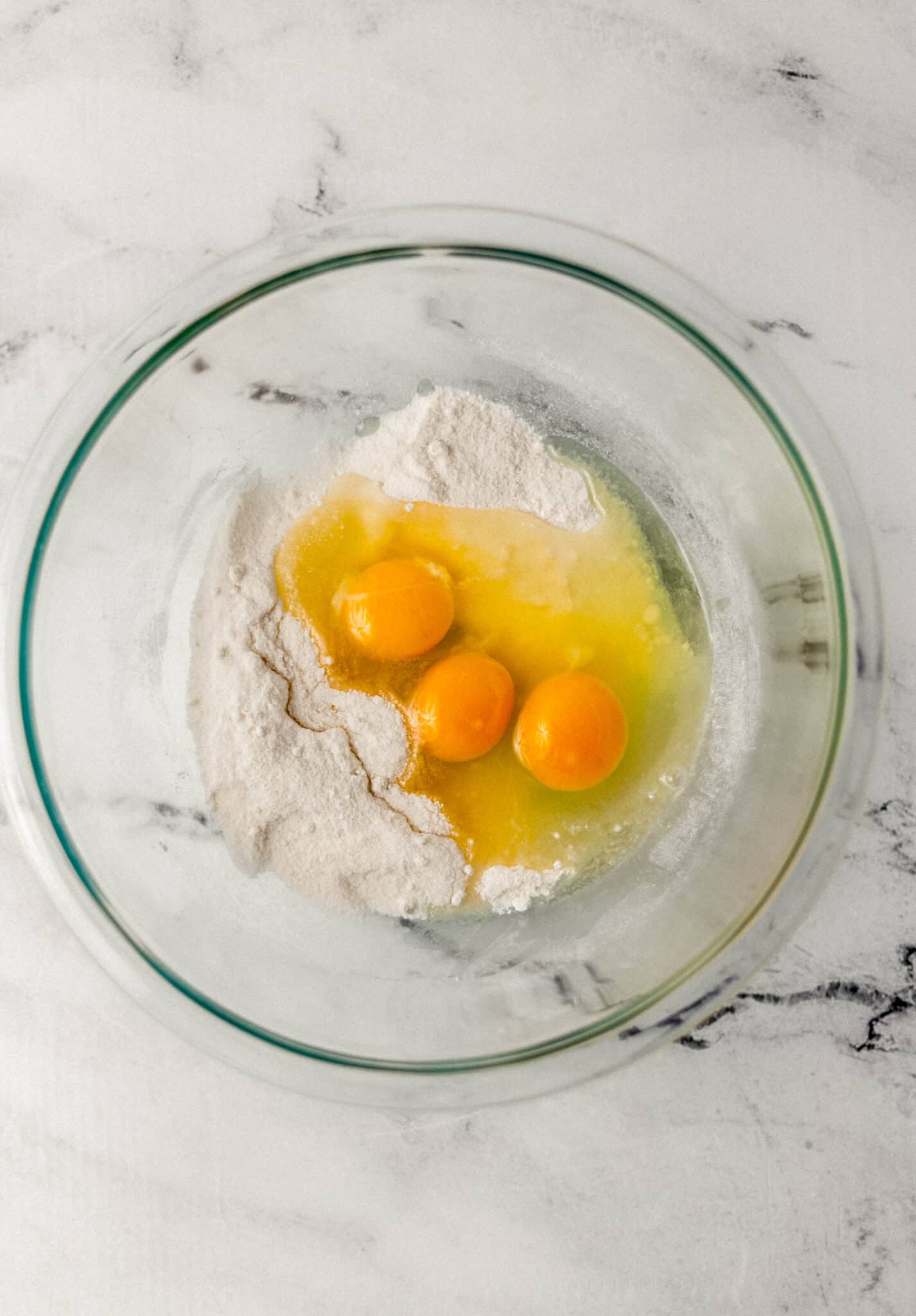 eggs added to glass mixing bowl with sugar and flour 