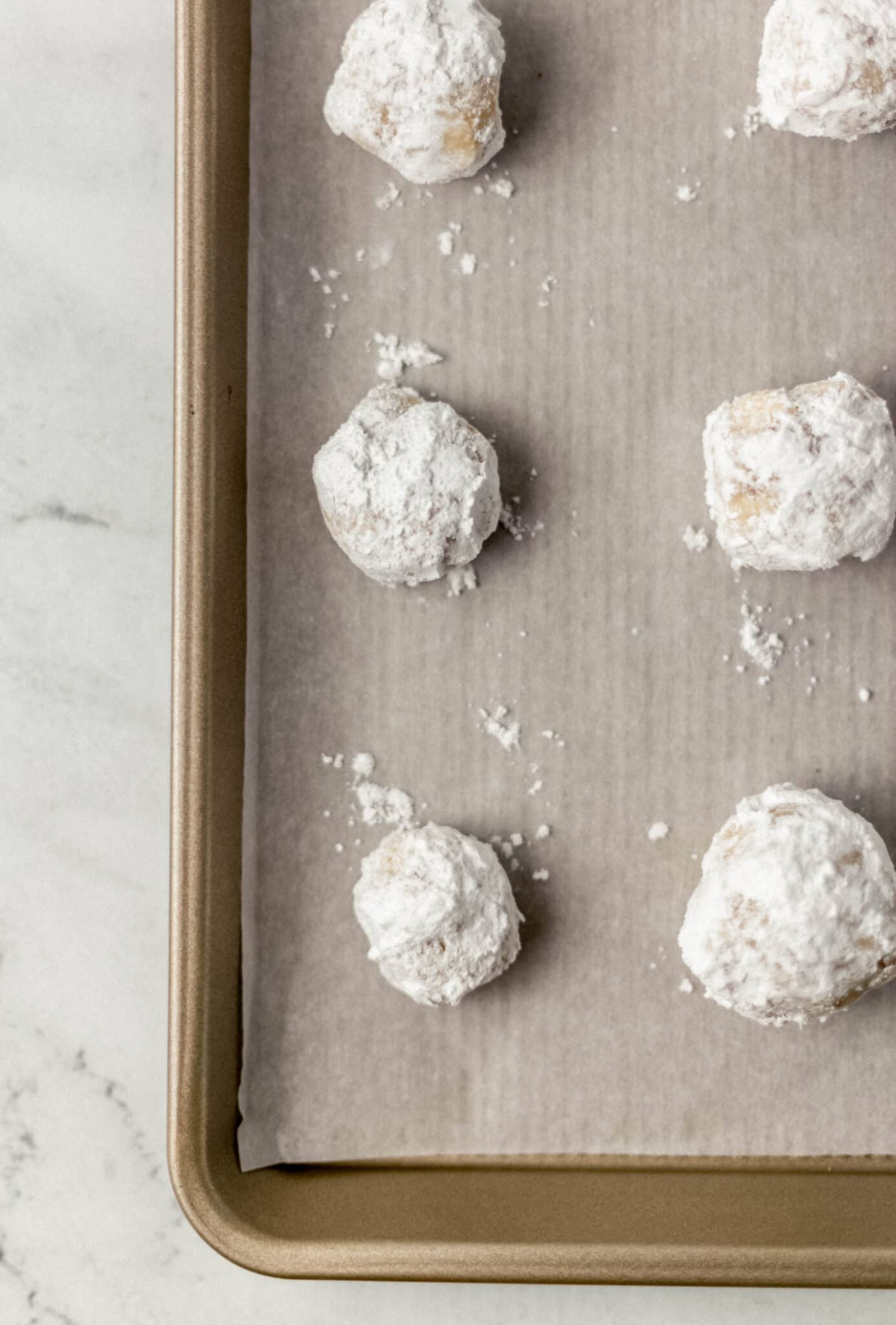 tea cakes rolled in powdered sugar on a parchment lined baking sheet before baking 