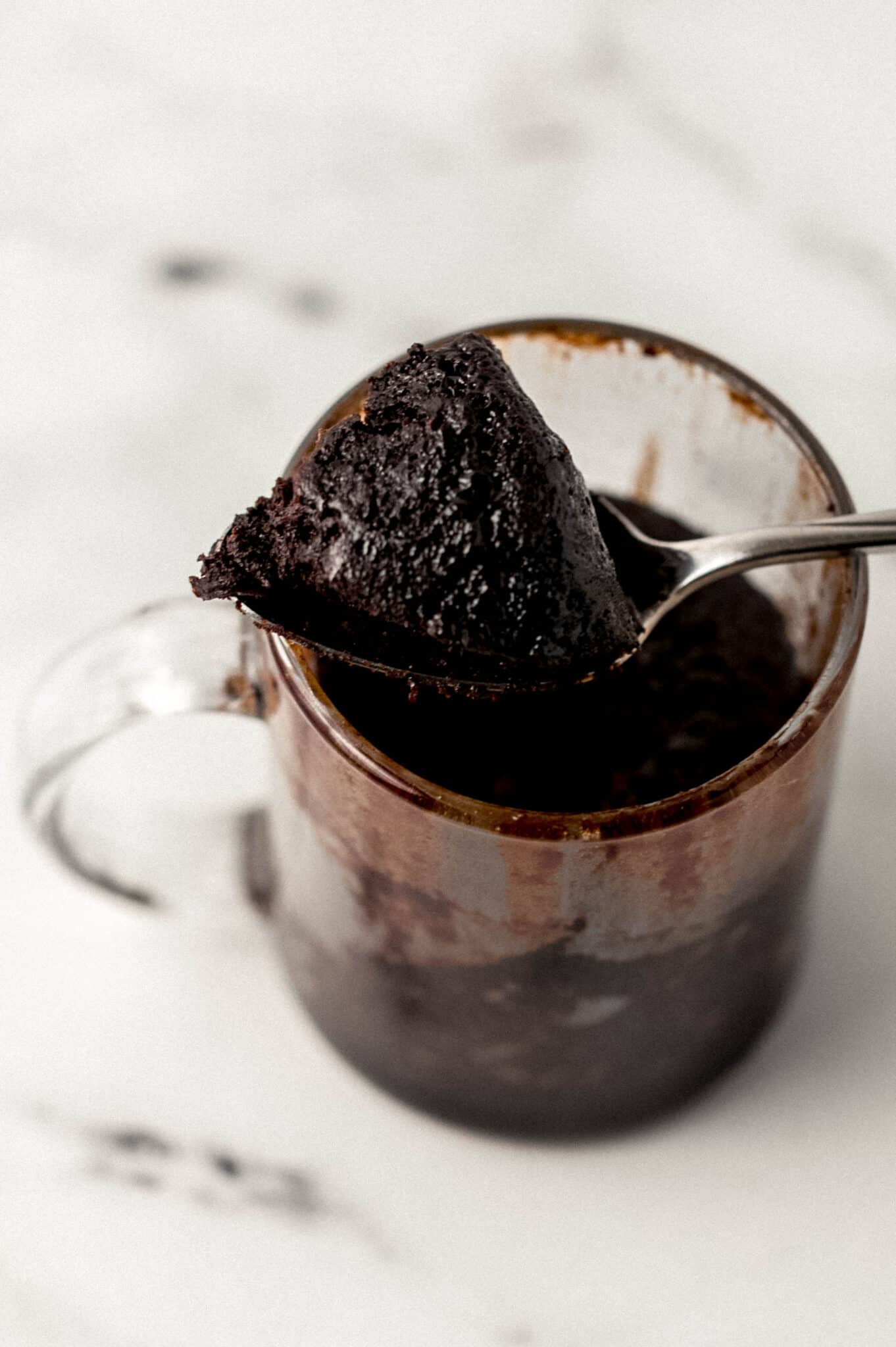 brownie in glass mug with spoon full of brownie over it 
