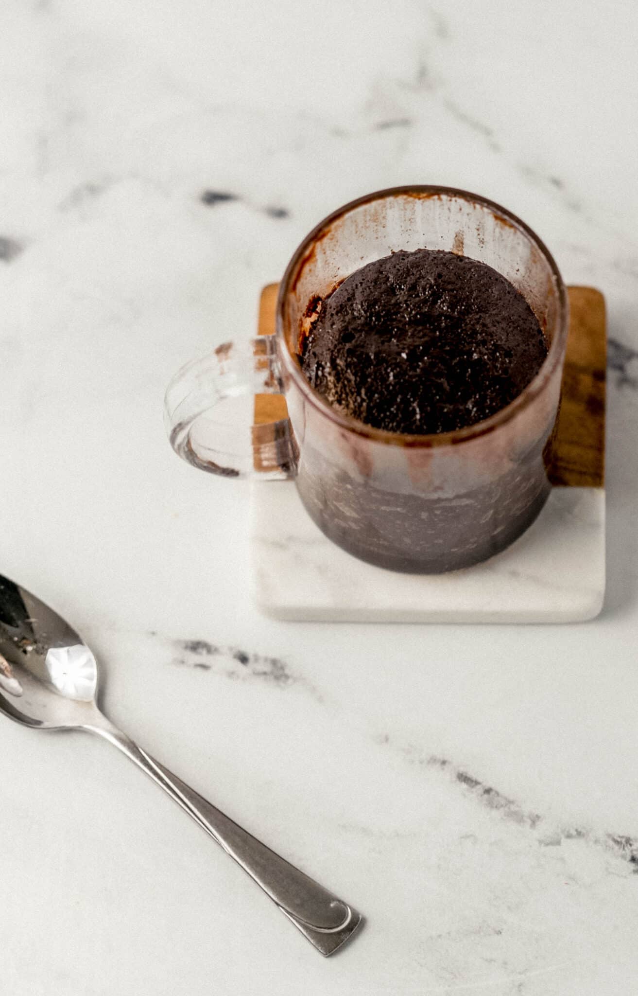 close up side view of finished mug brownie on coaster beside a spoon 