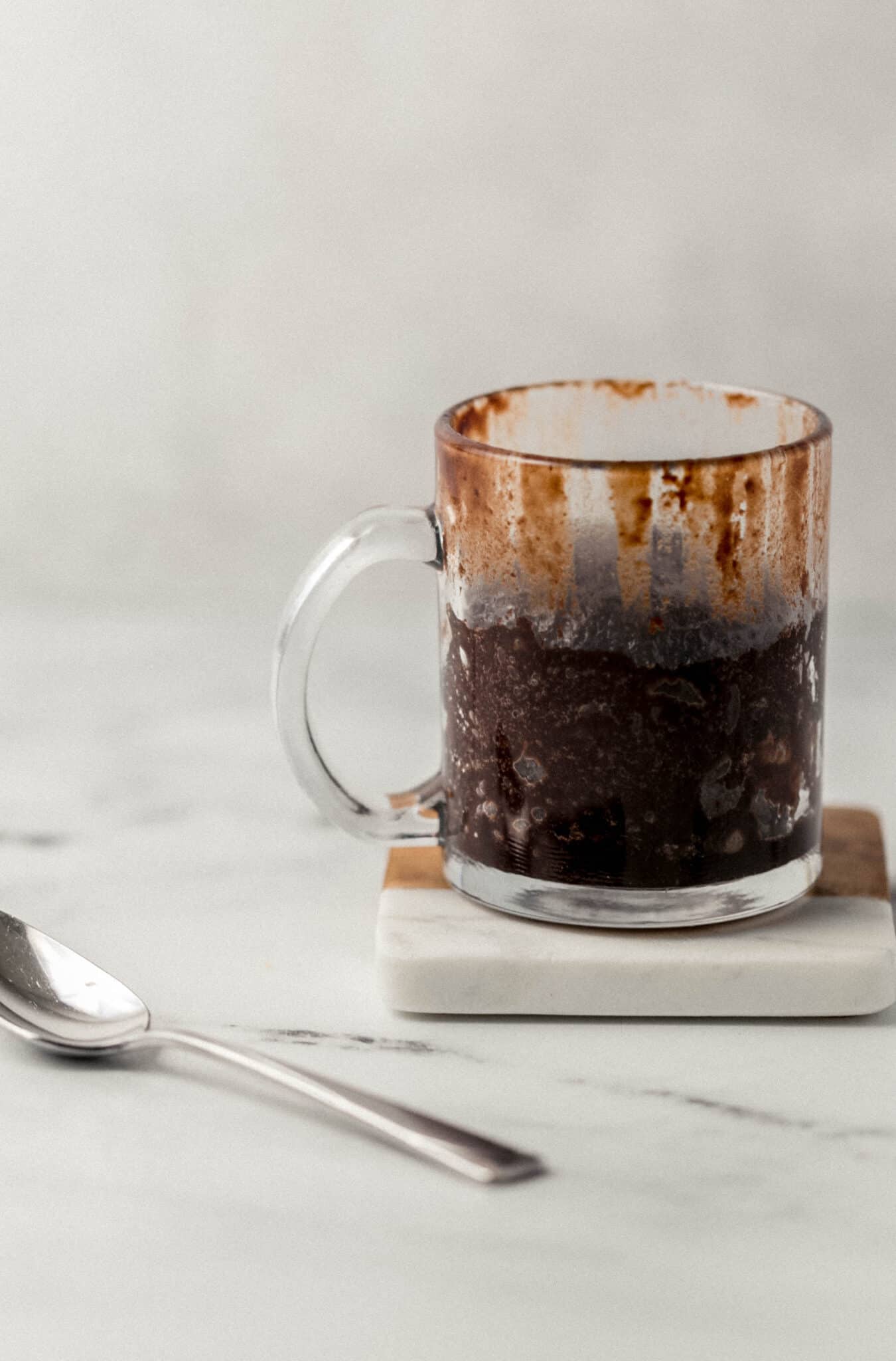 close up side view of finished brownie in mug on coaster beside a spoon 