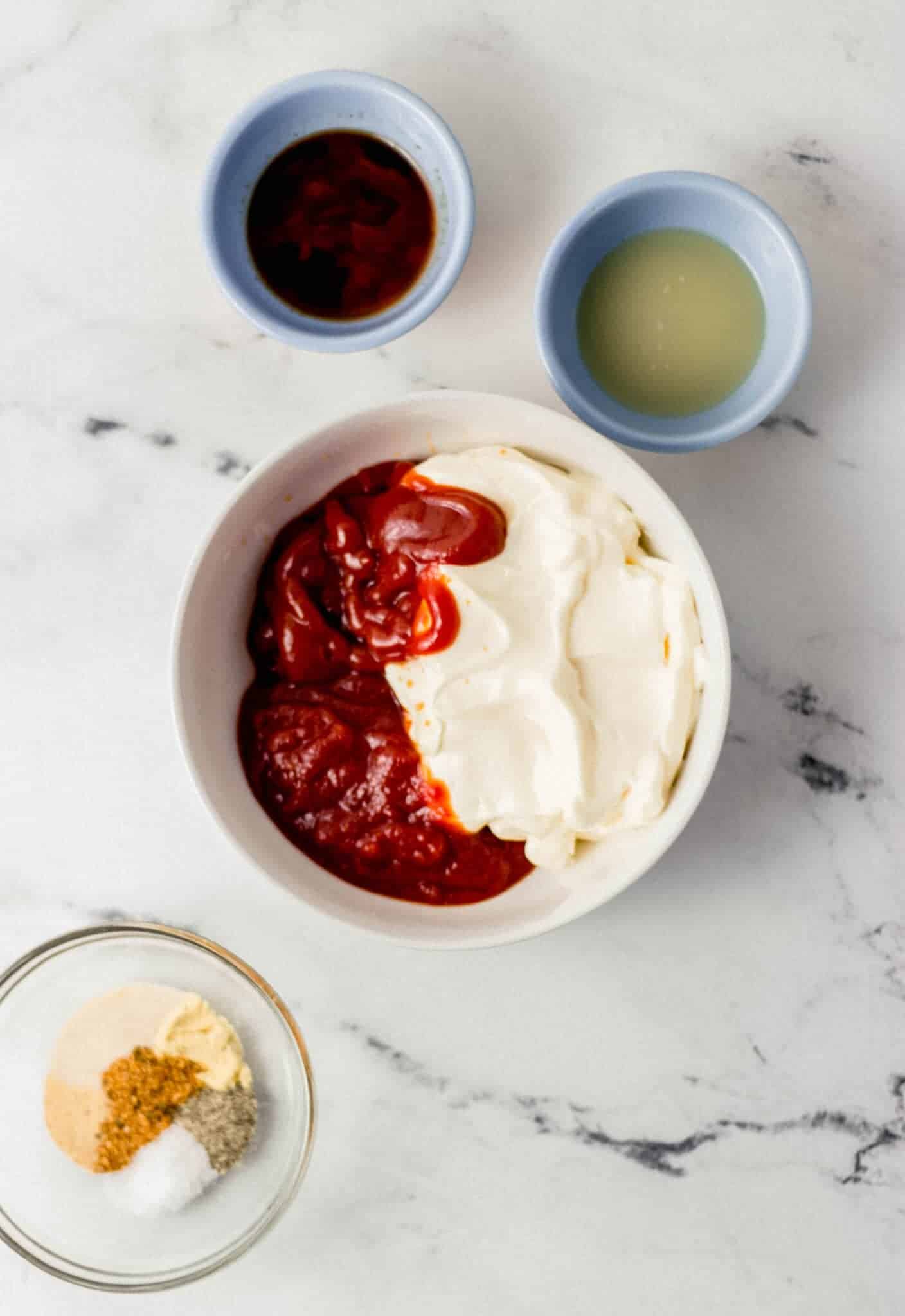 overhead view of ingredients needed to make sauce in separate bowls on marble surface 