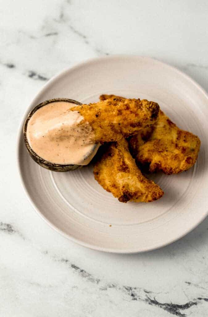 overhead view of a small plate with chicken fingers on it and a small wooden bowl with comeback sauce in it