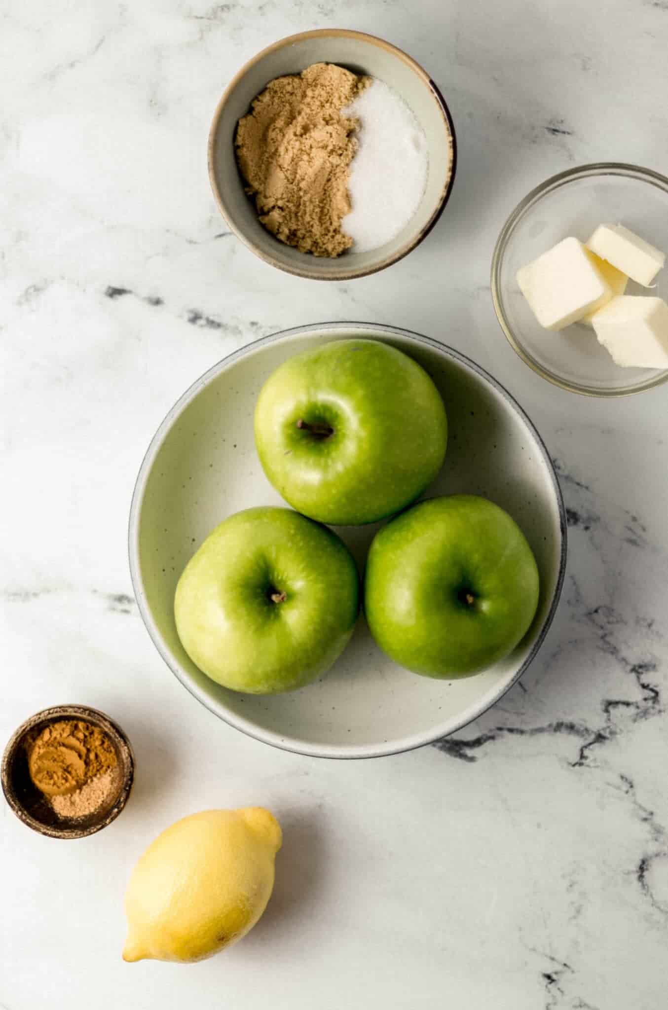 overhead view of ingredients needed to make fried apples in separate bowls on marble surface 