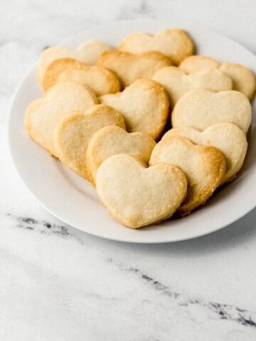 close up side view of white plate of heart shaped shortbread cookies
