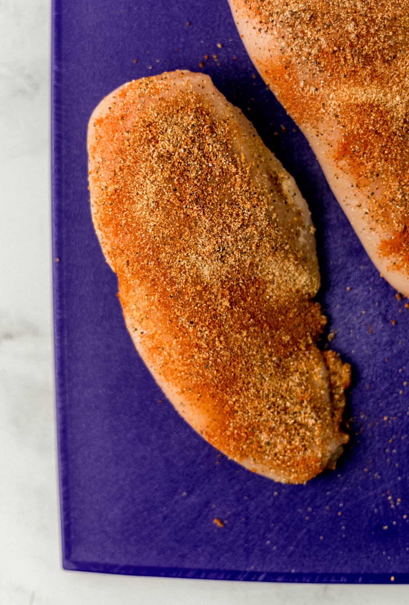 seasoned uncooked chicken breast on blue cutting board 