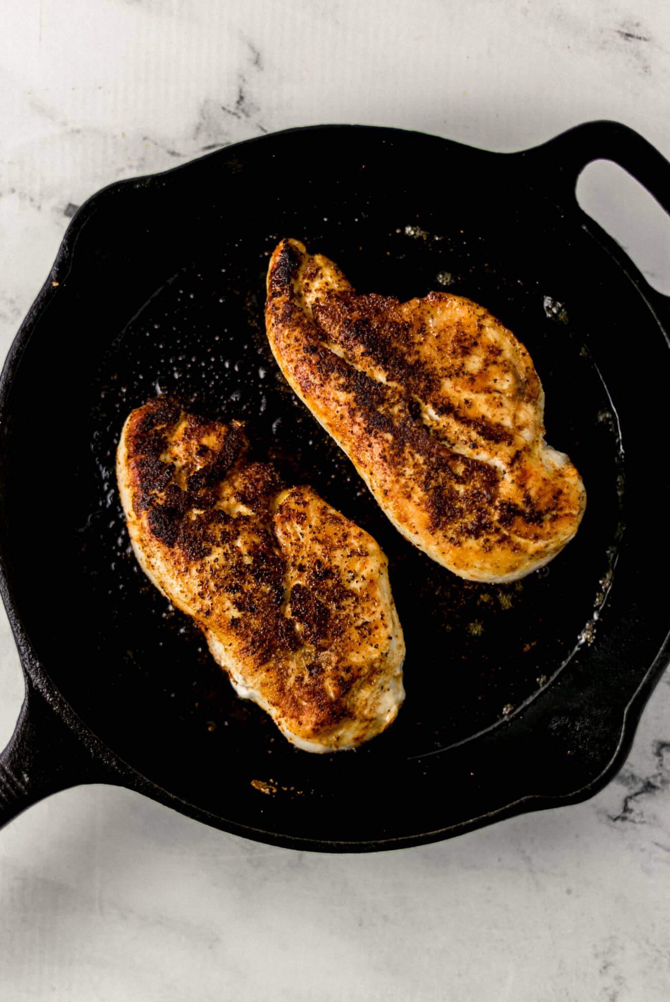 two pieces of chicken breast in cast iron skillet turned over to opposite side before placing into the oven