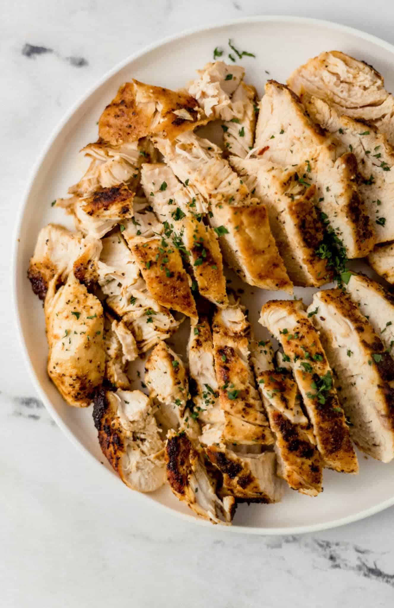 finished chicken breast on white plate topped with chopped fresh parsley 