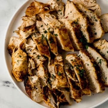 overhead view of sliced chicken breast on white plate topped with chopped parsley