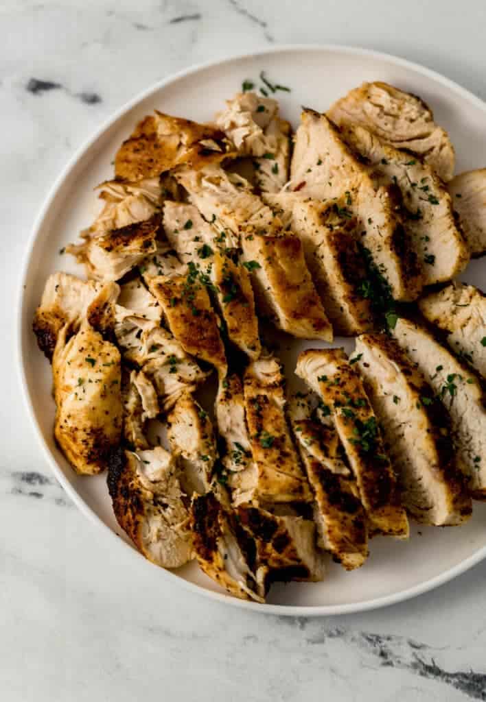 overhead view of sliced chicken breast on white plate topped with chopped parsley