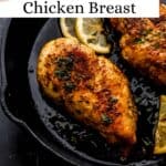 Close up front view of chicken breast in skillet with lemon slices on pin with text overlay.