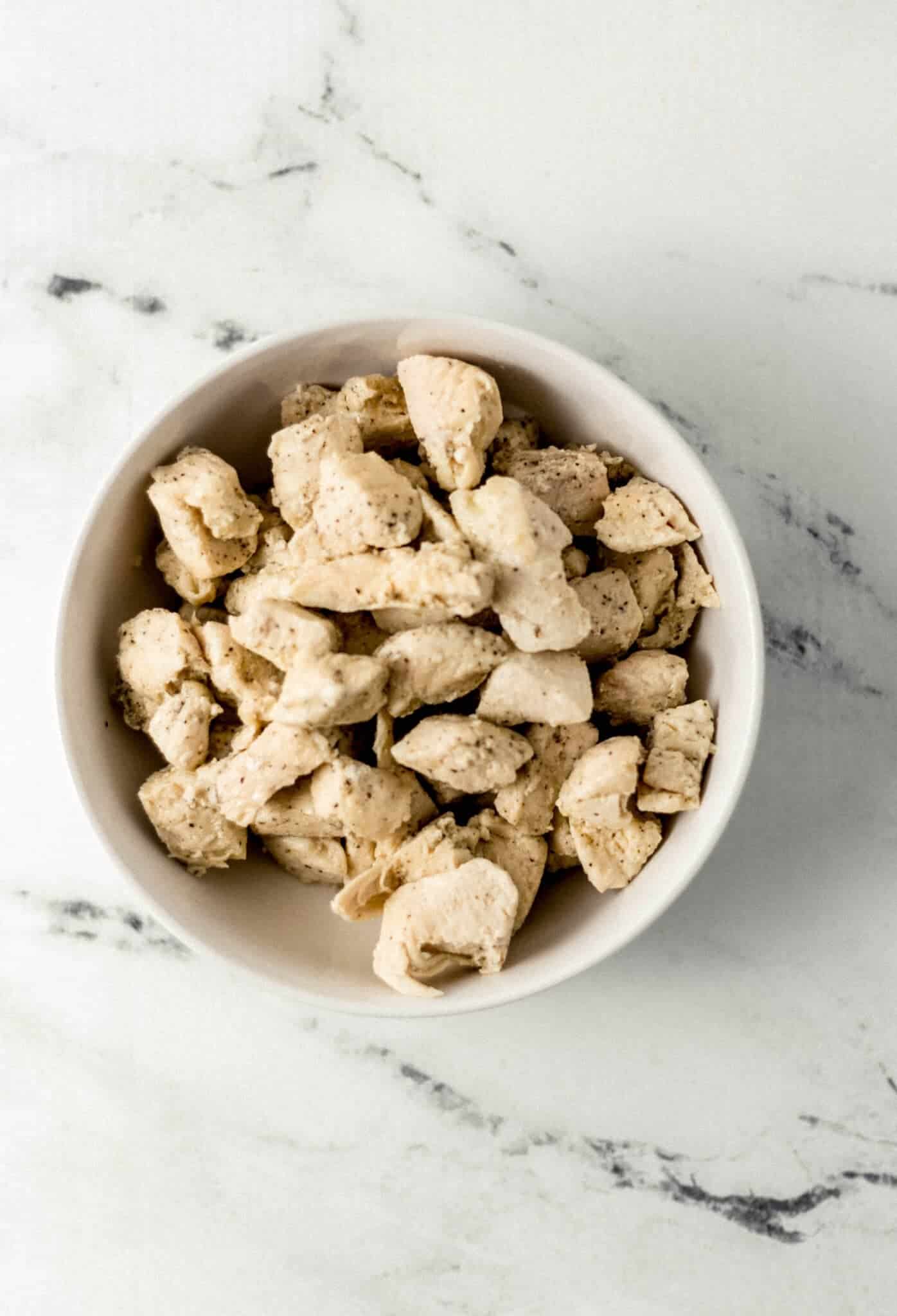 white bowl with cooked and cut up chicken in it on marble surface 