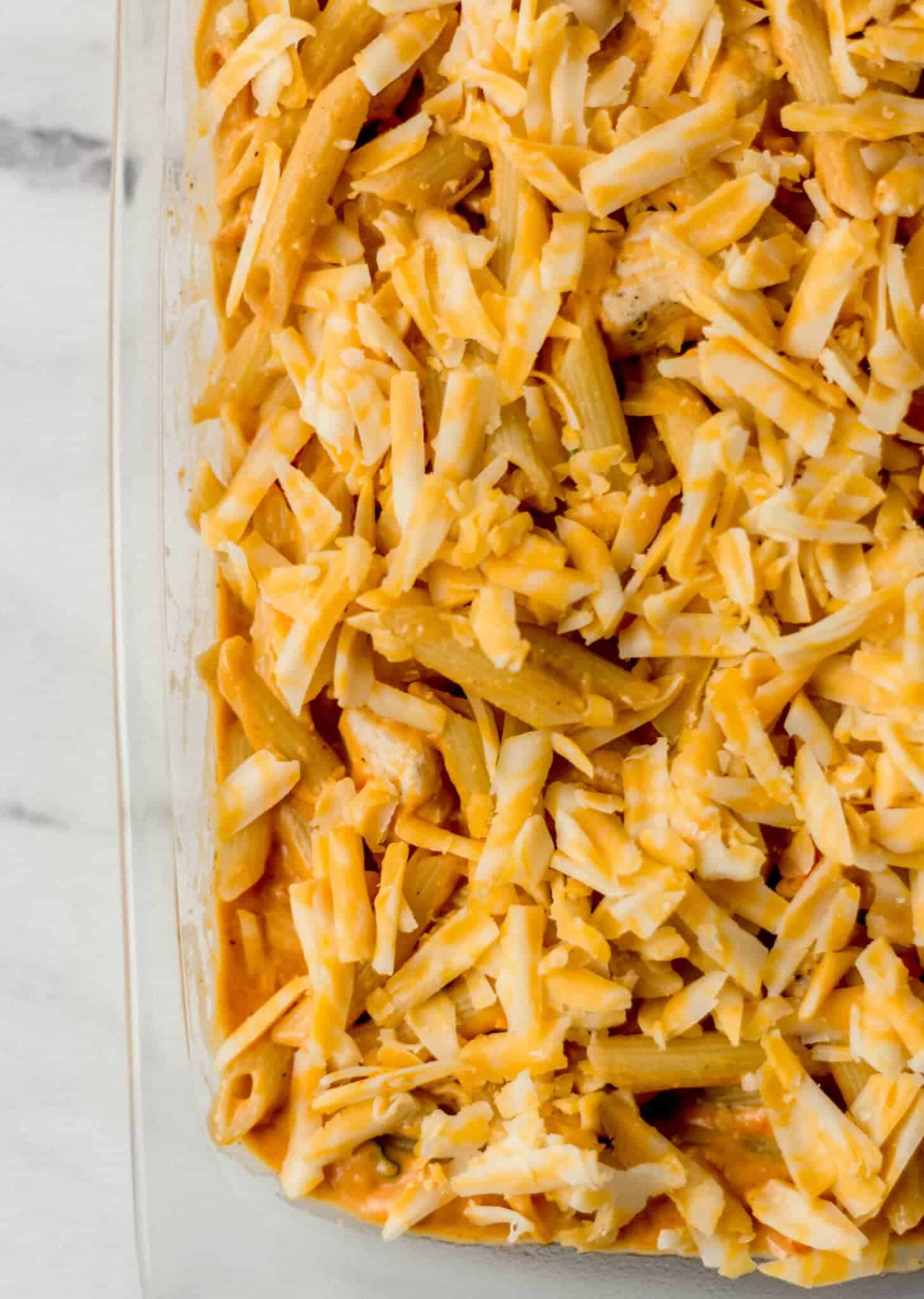 pasta topped with shredded cheese in glass baking dish 