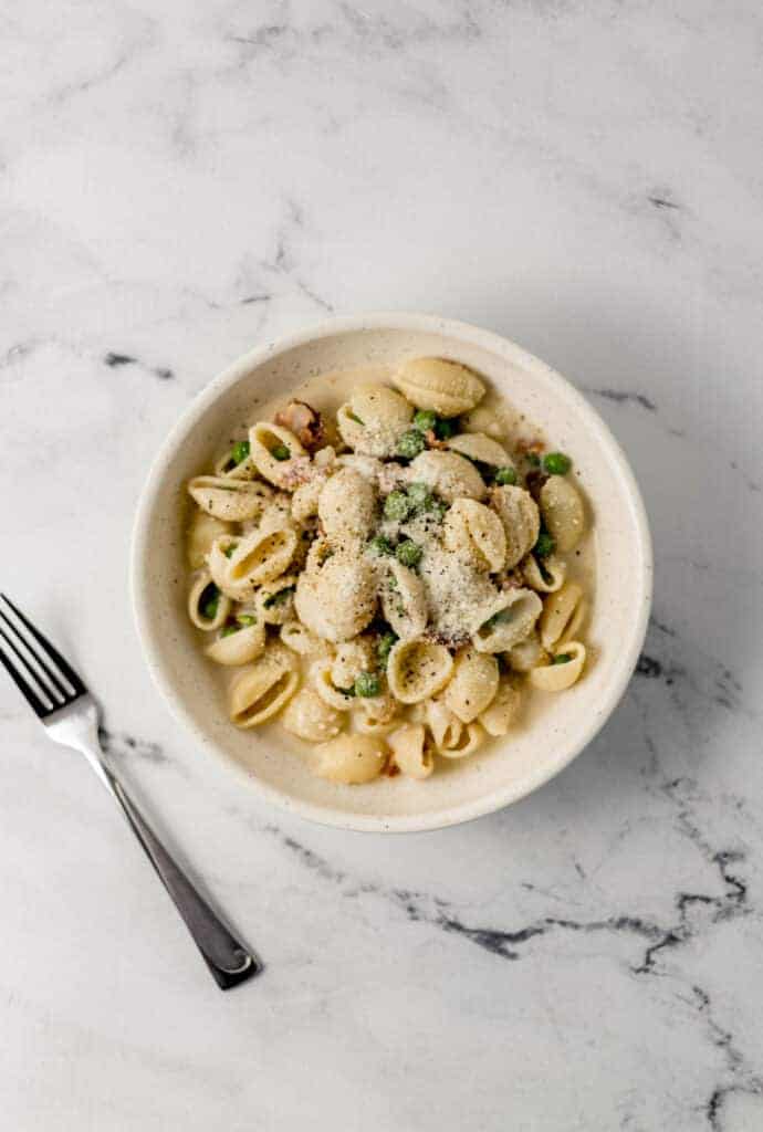 overhead view of bowl of alfredo pasta topped with parmesan beside a fork