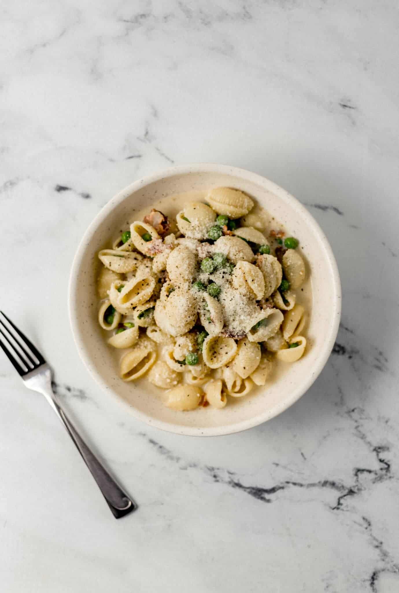 overhead view of bowl of alfredo pasta topped with parmesan beside a fork 