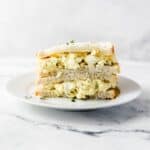 Close up side view of egg salad sandwich on white plate.