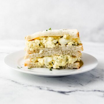 Close up side view of egg salad sandwich on white plate.