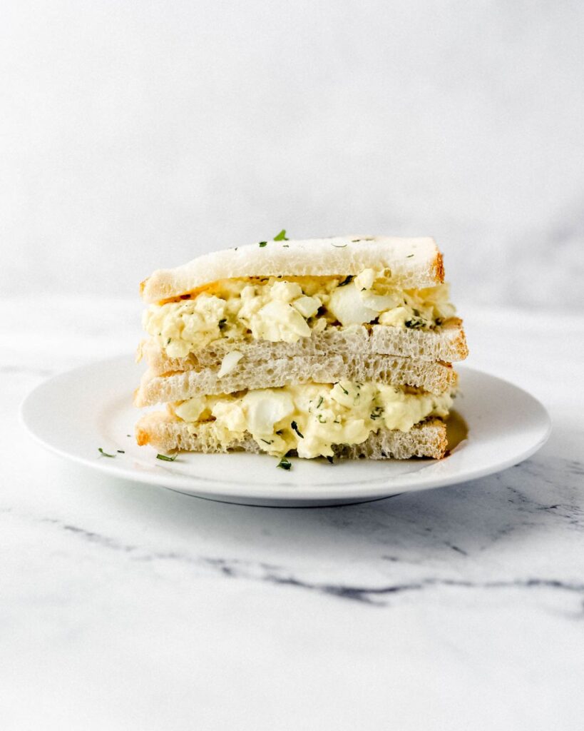 Close up side view of egg salad sandwich on white plate.