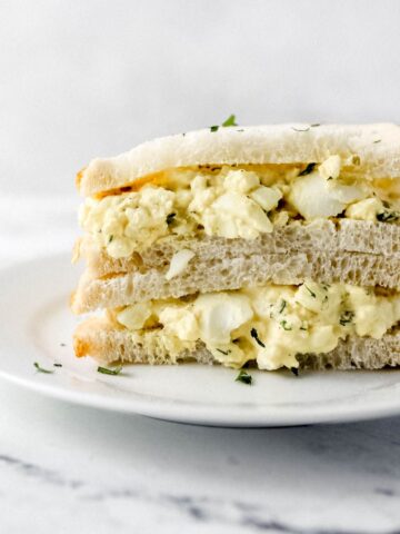 Close up side view of egg salad sandwich on white plate.