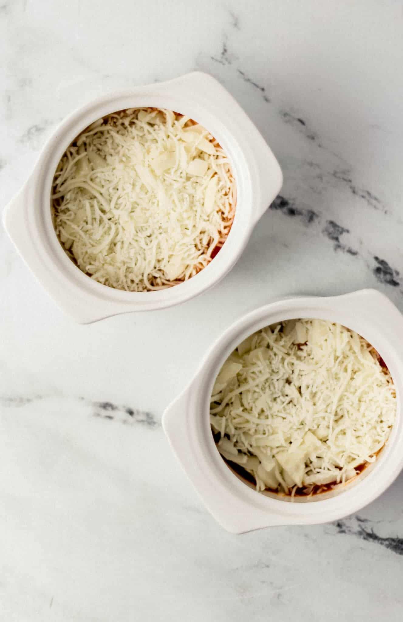 two white ramekins with sauce and shredded cheese in them