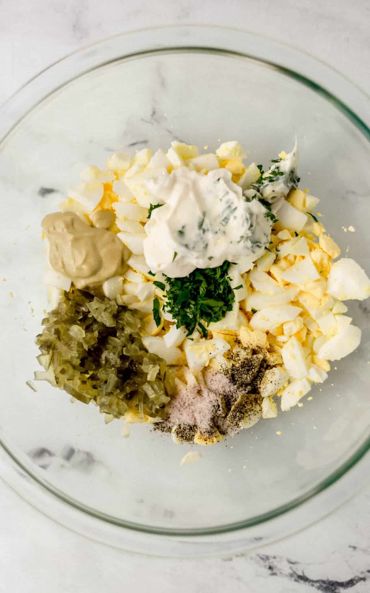 egg salad ingredients added to large glass bowl 