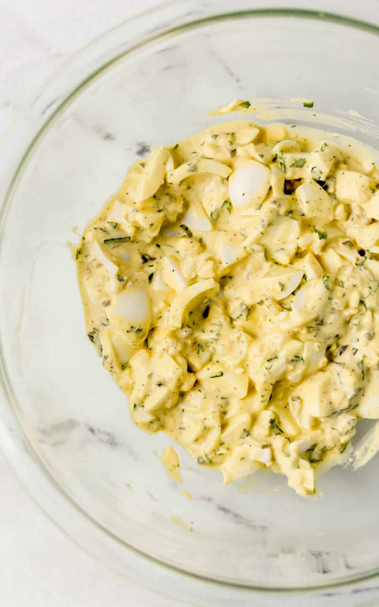 egg salad ingredients combined in glass mixing bowl 