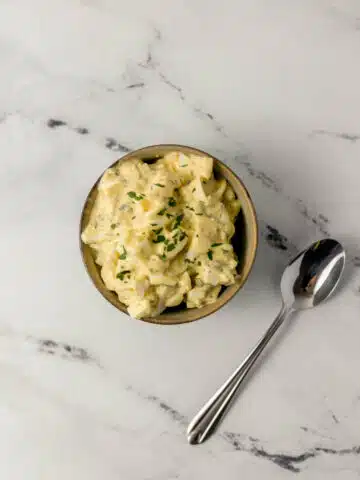 overhead view of egg salad in a bowl beside a spoon on marble surface