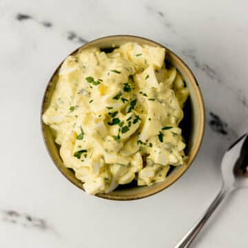 egg salad in a bowl beside a spoon on marble surface