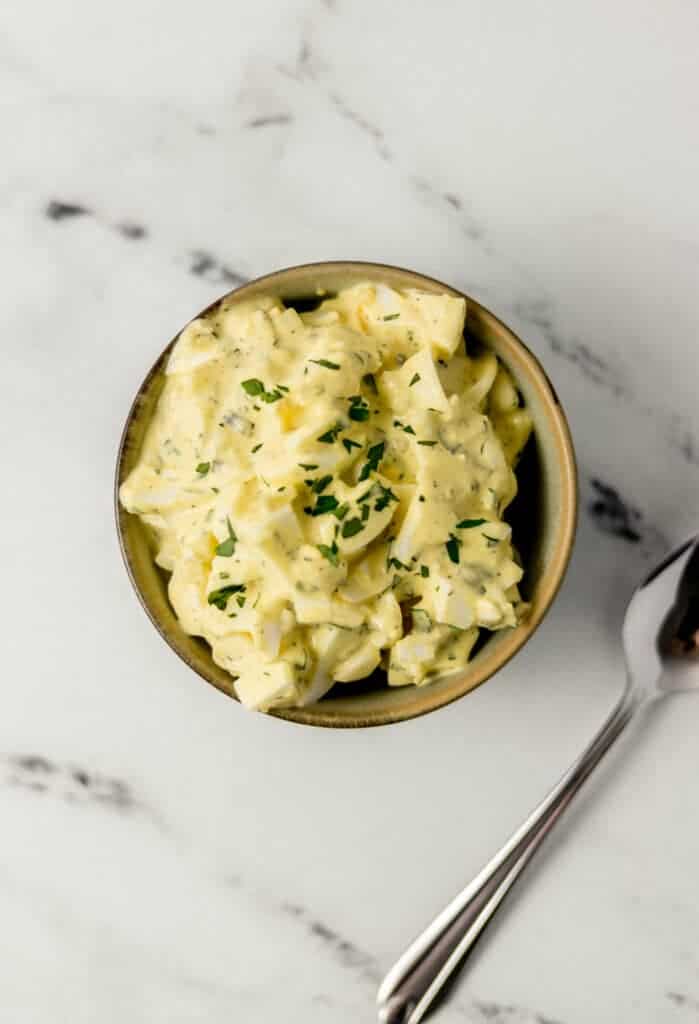 egg salad in a bowl beside a spoon on marble surface