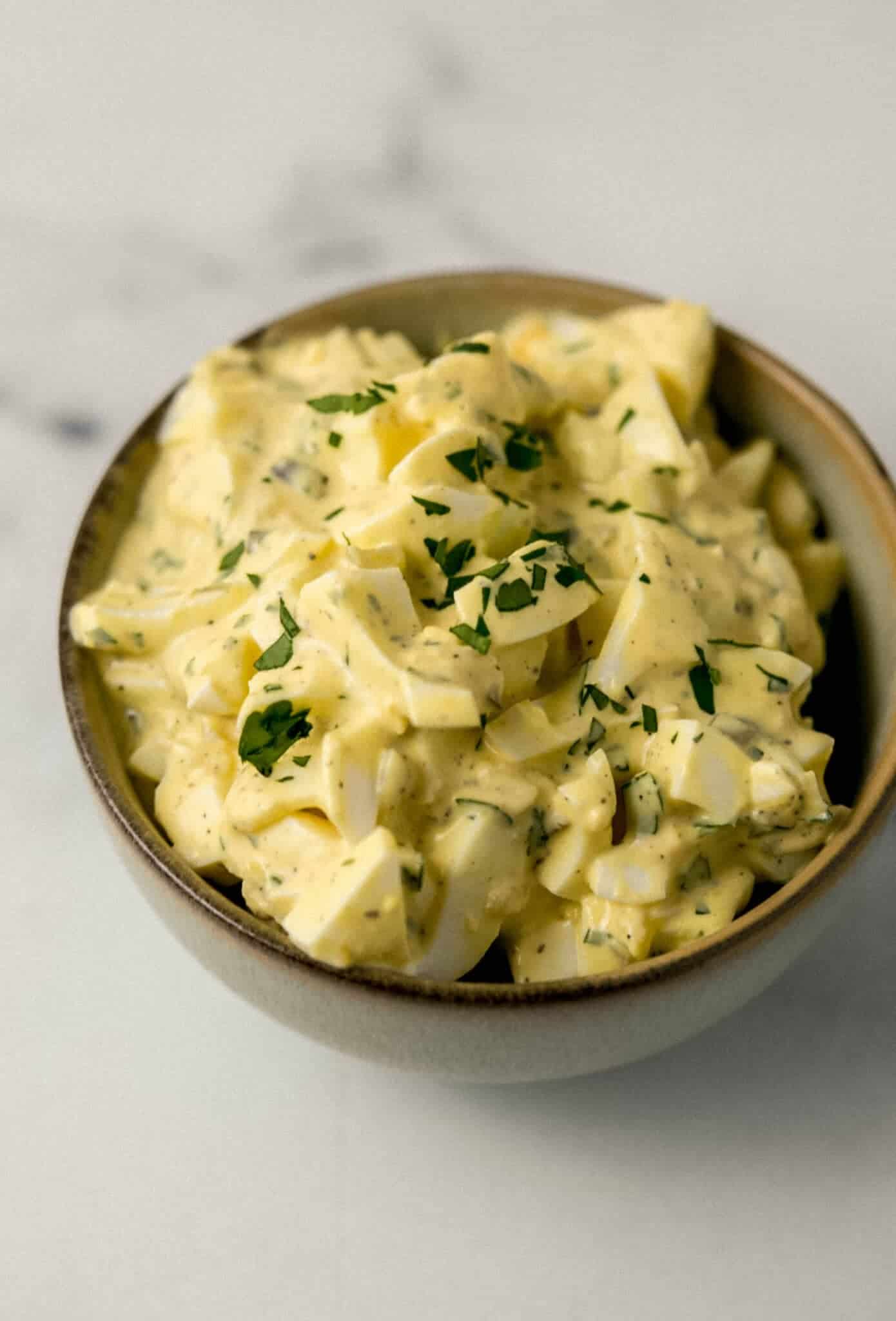 close up side view of finished egg salad topped with chopped parsley in small bowl 