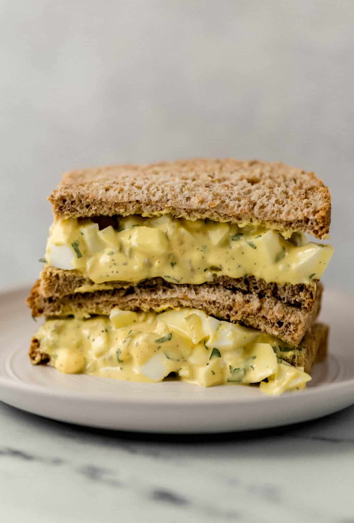 close up side view of egg salad sandwich on white plate 