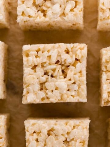 Close up overhead view of rice krispie treats cut into squares on parchment paper.