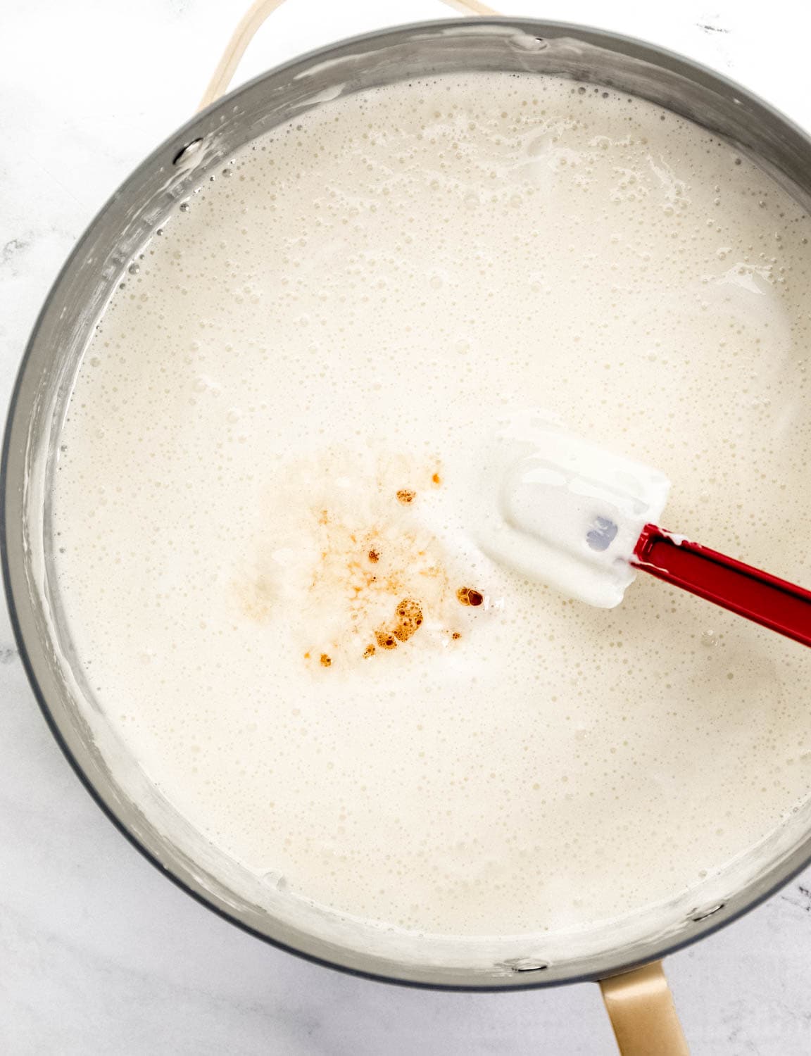 Vanilla extract added to melted marshmallow mixture in large pot with spatula.