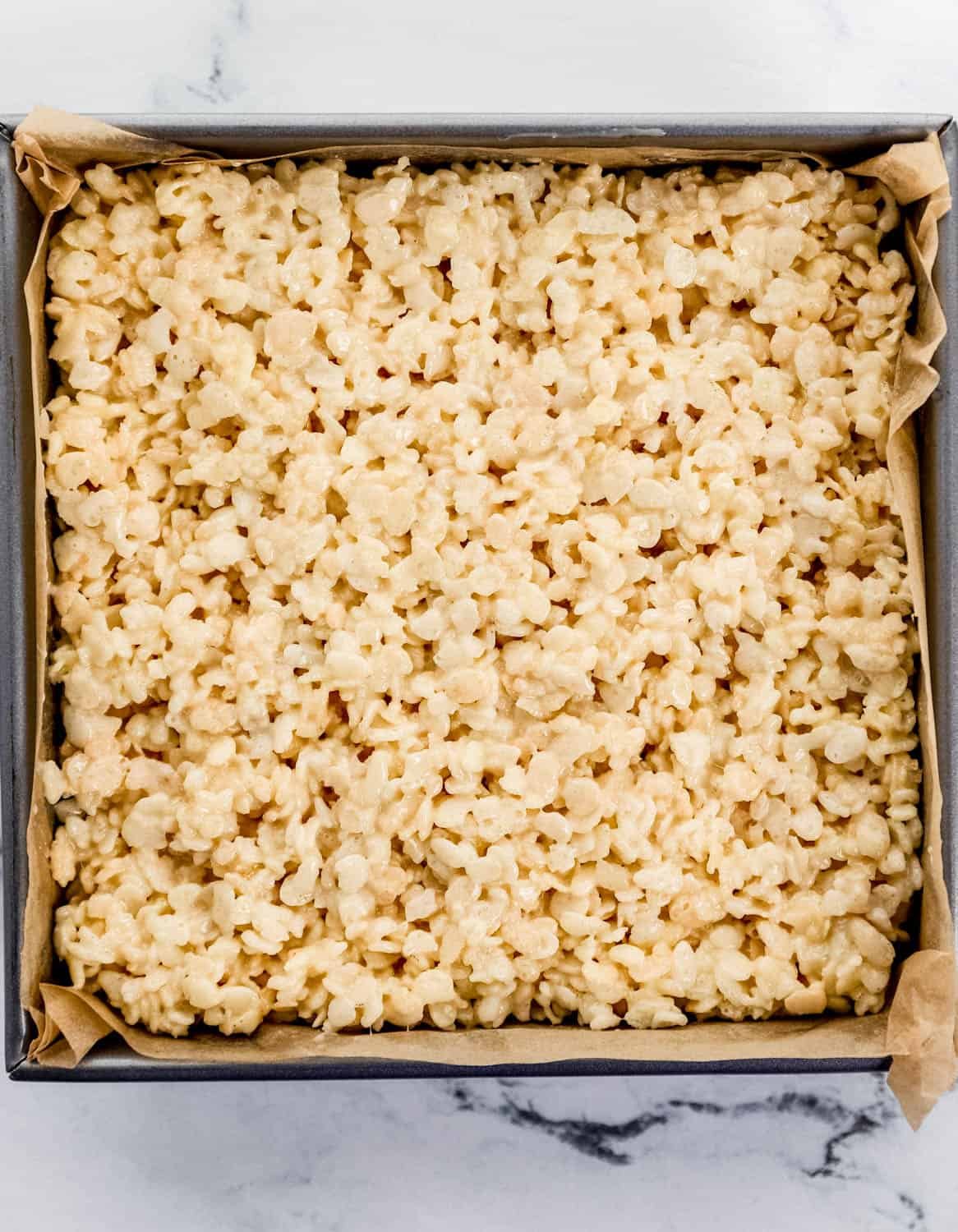 Overhead view of rice krispie treats in parchment lined square baking sheet.