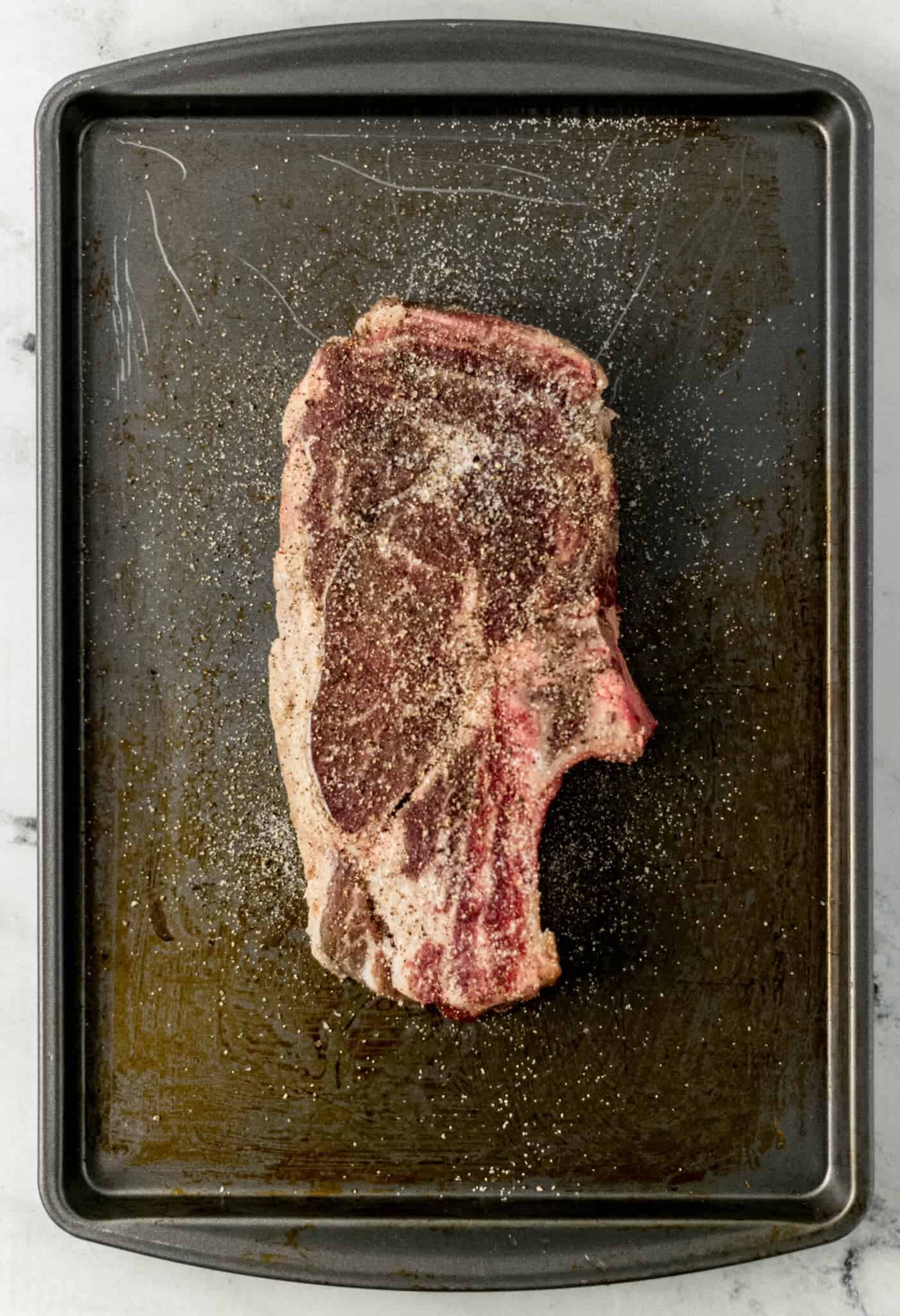 seasoned raw steak on baking sheet