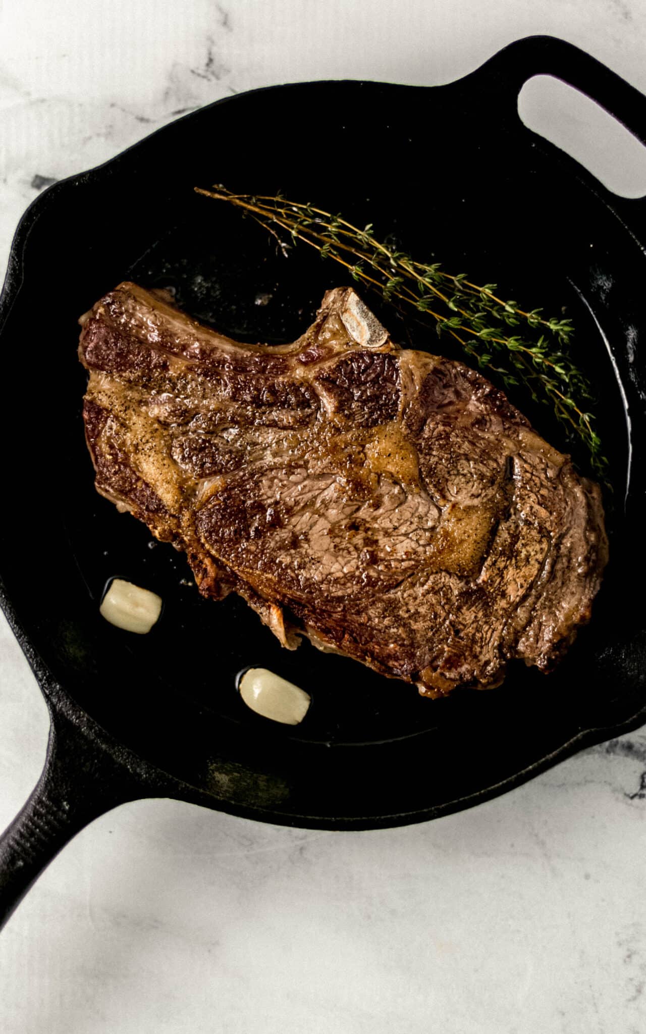 steak flipped over to other side in cast iron skillet with hot oil, fresh thyme, and two garlic cloves. 