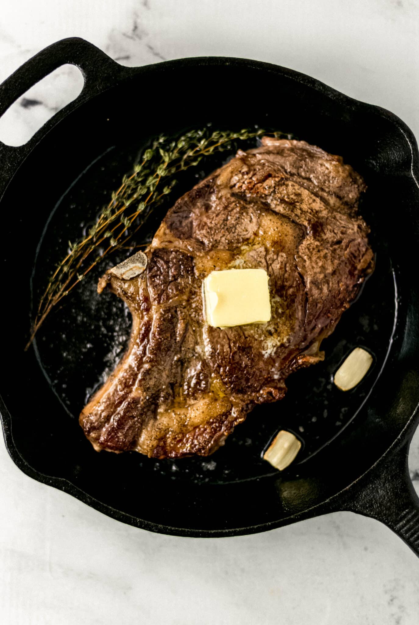 cooked steak topped with butter in cast iron skillet with garlic cloves and thyme