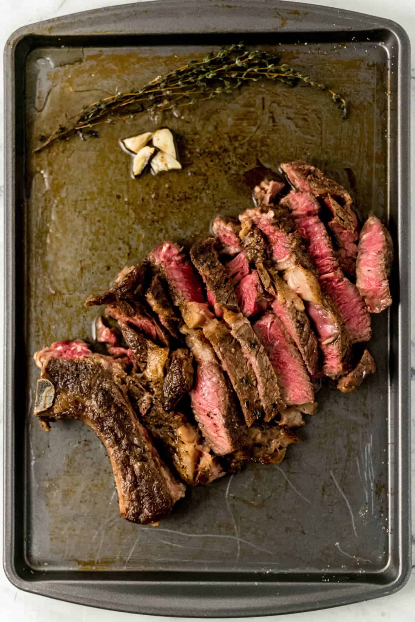 cut steak on baking sheet with garlic cloves and thyme 