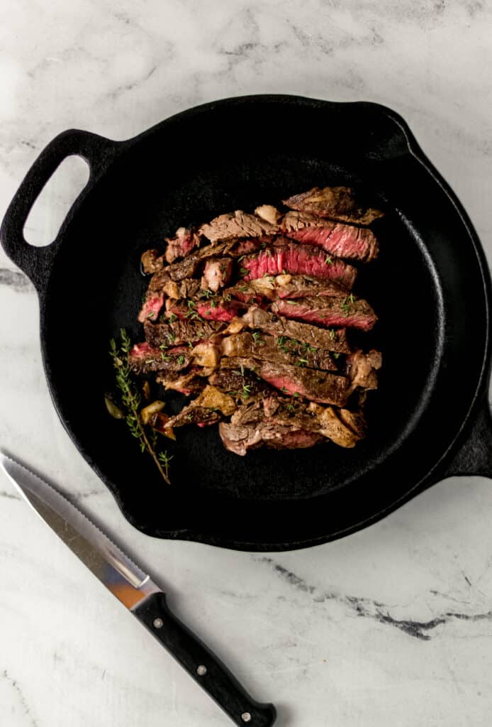 finished and cut ribeye steak in cast iron skillet topped with thyme beside a knife