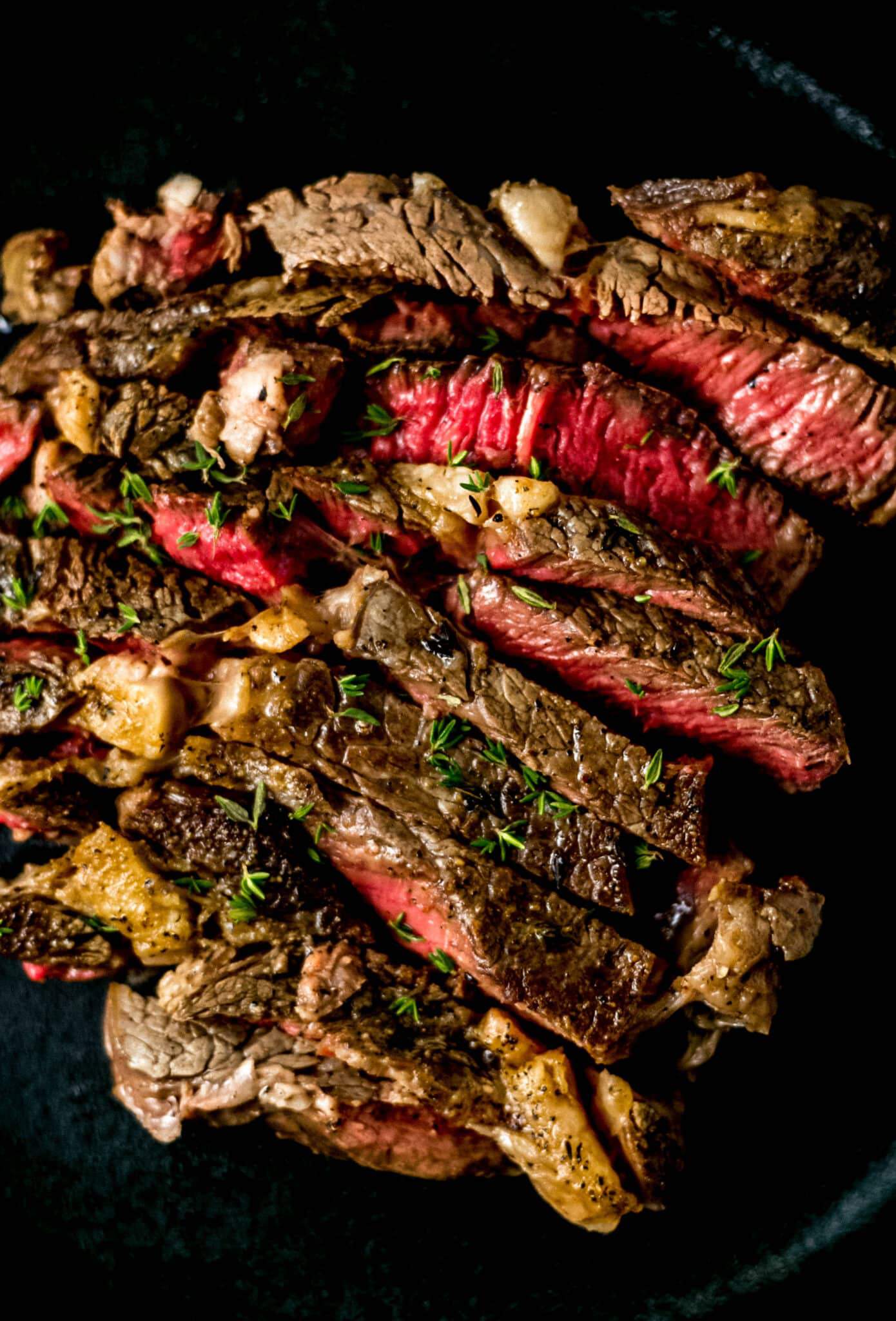 close up view of cut steak in cast iron skillet topped with fresh thyme 