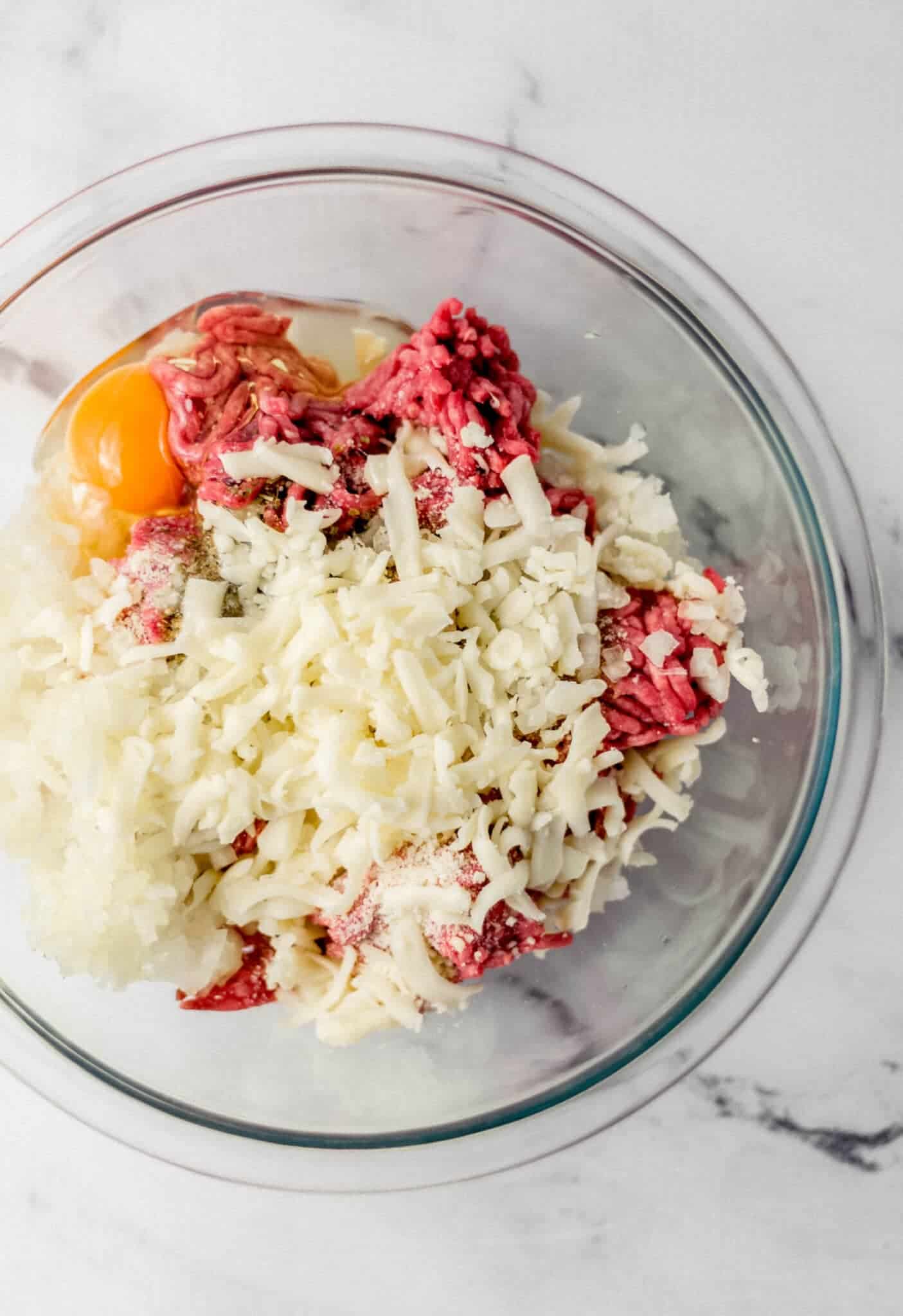 ingredients to make meatballs added to glass mixing bowl 