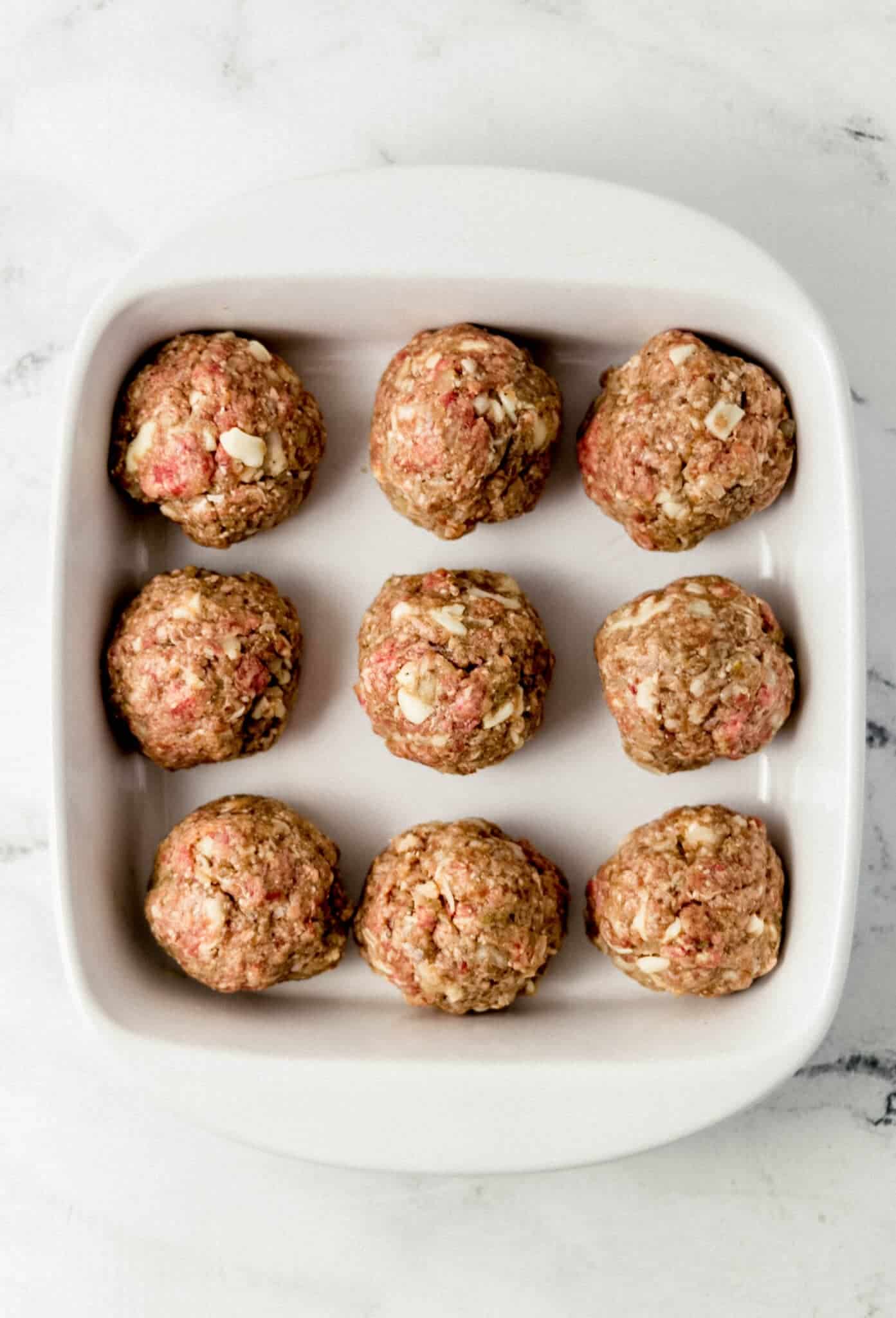 uncooked meatballs place in white baking dish