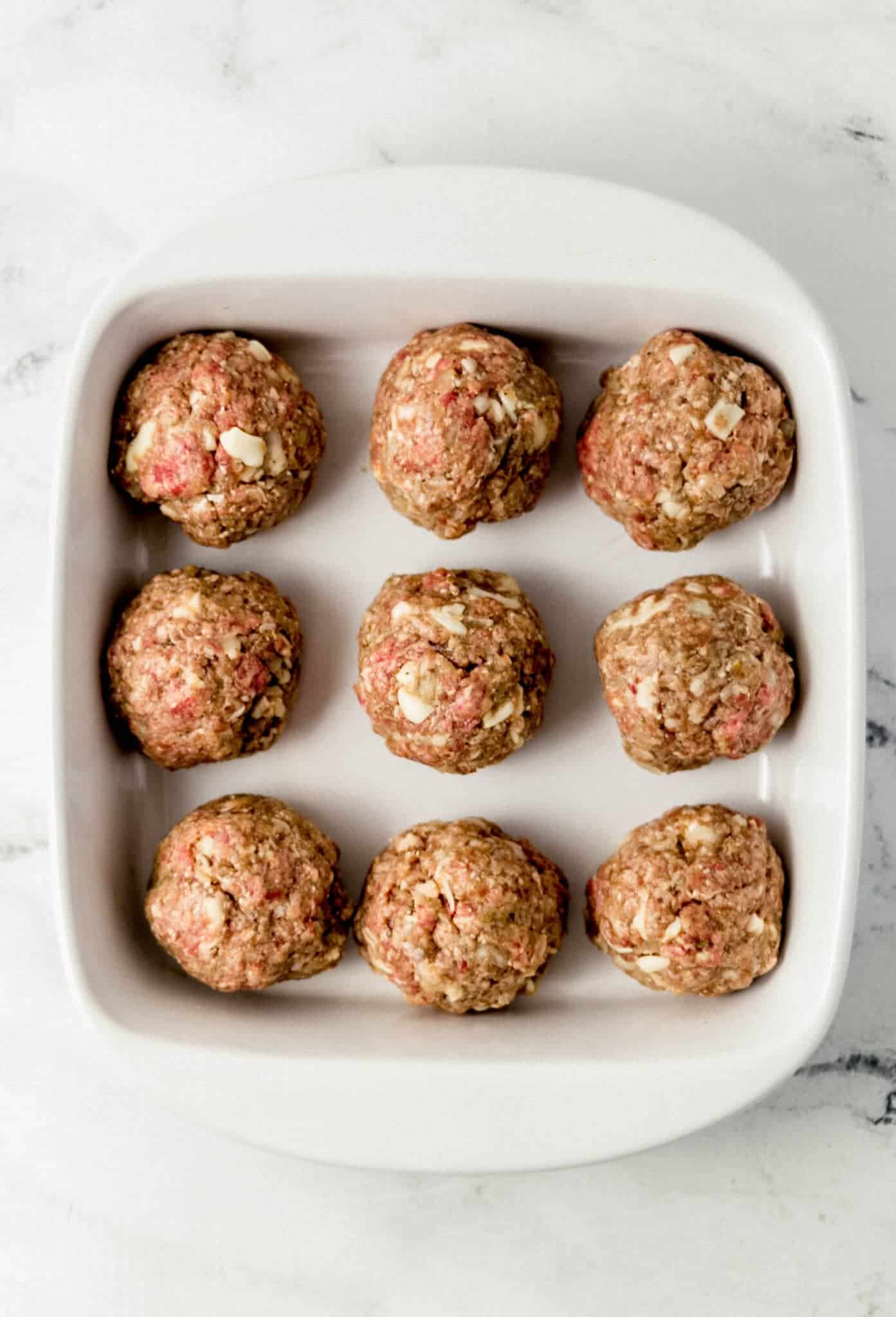 uncooked meatballs place in white baking dish 