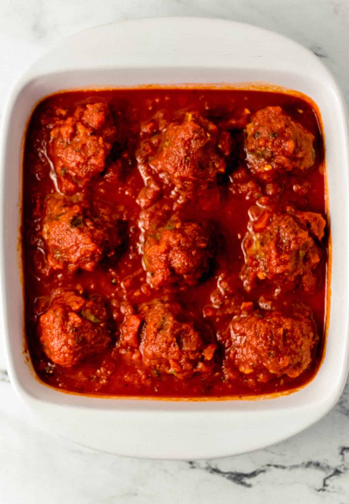 meatballs topped with sauce in white baking dish