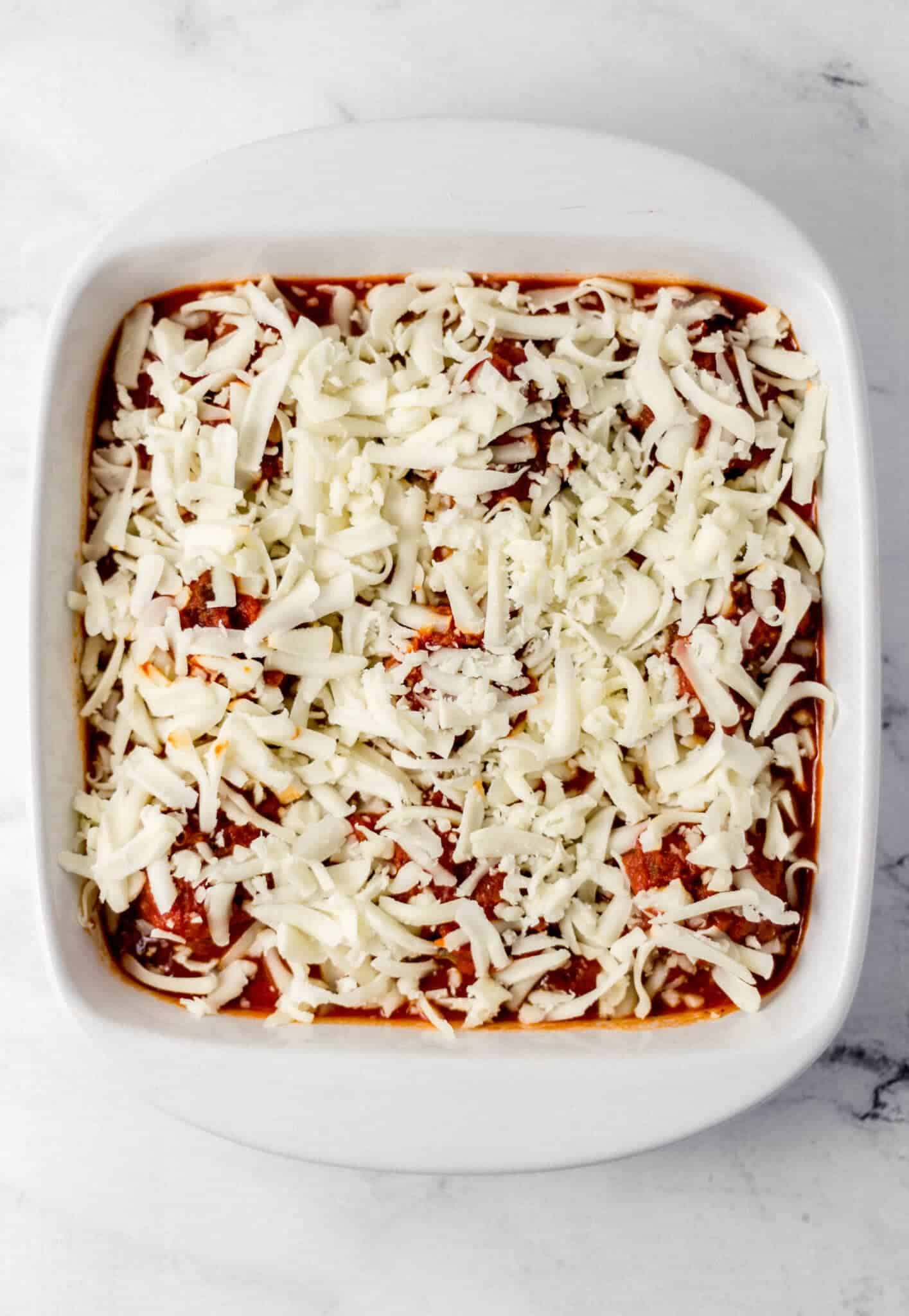 meatballs and sauce topped with shredded cheese in white baking dish 